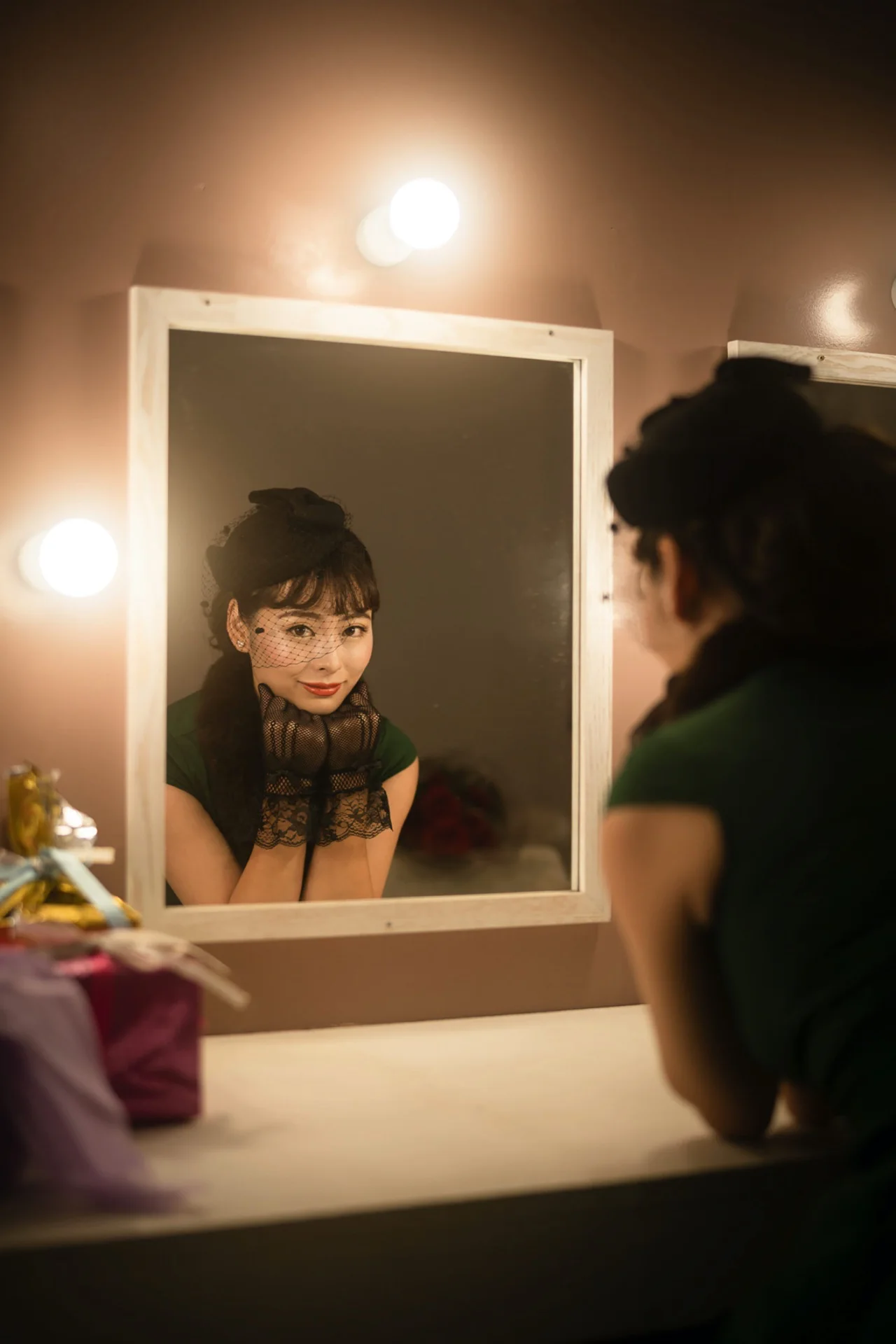 A performer at a dressing room mirror ringed with bulbs, each bulb glowing softly