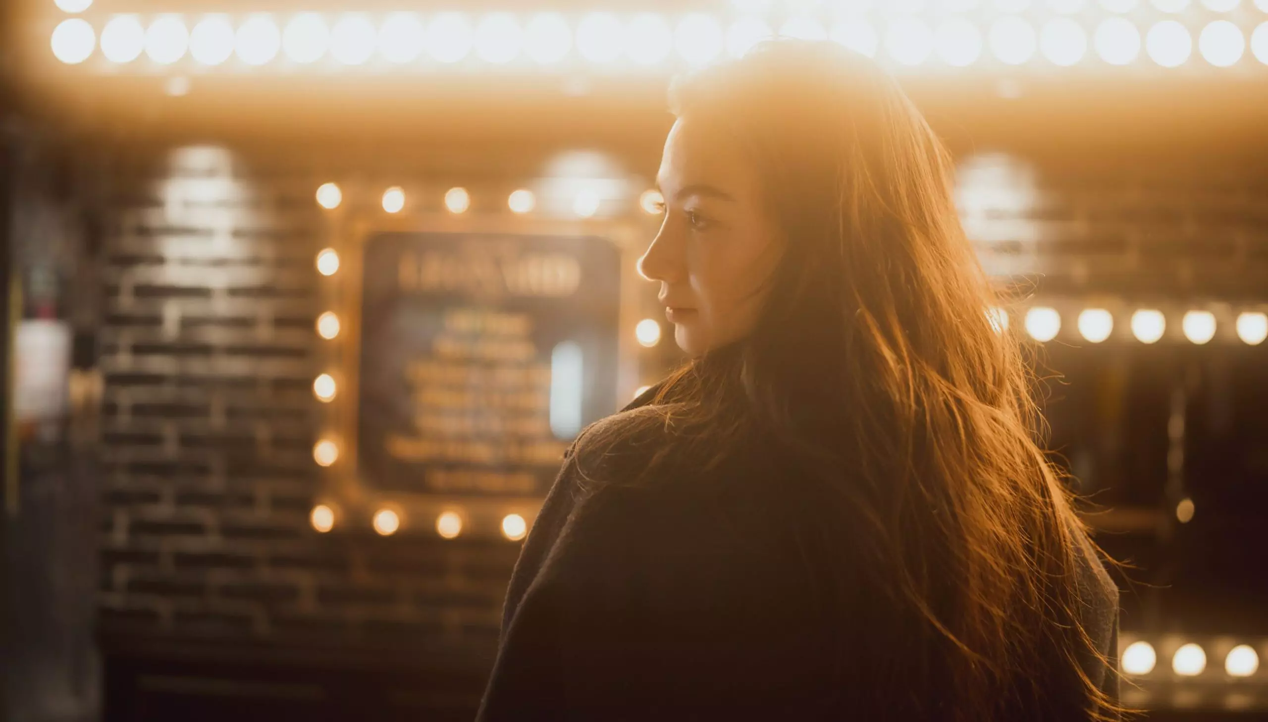 A woman silhouetted against a theater marquee of warm bulbs, the highlights held back