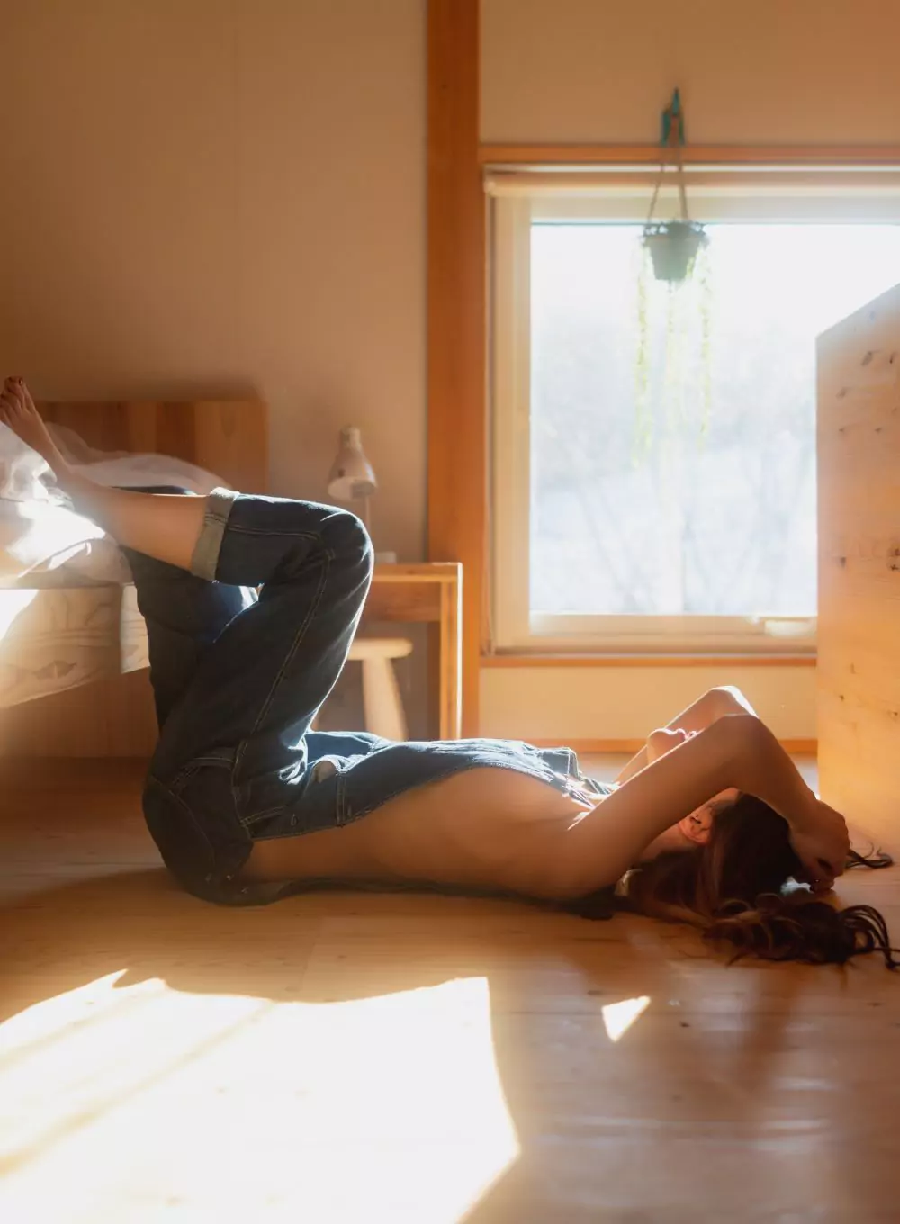 A woman lying on a wooden floor in warm window light, the light spilling across the boards