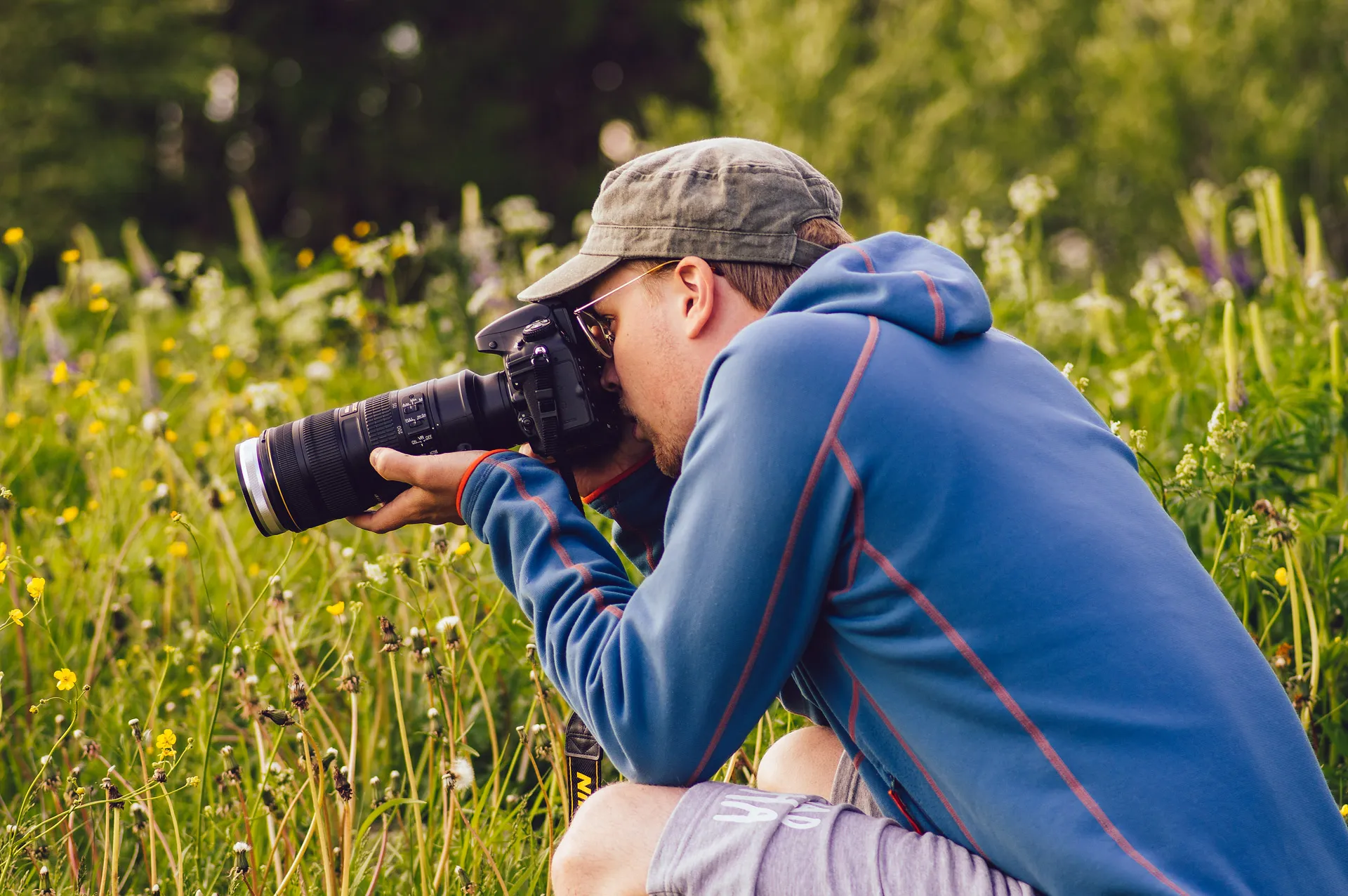 A photographer crouched in a wildflower meadow shooting with a telephoto lens