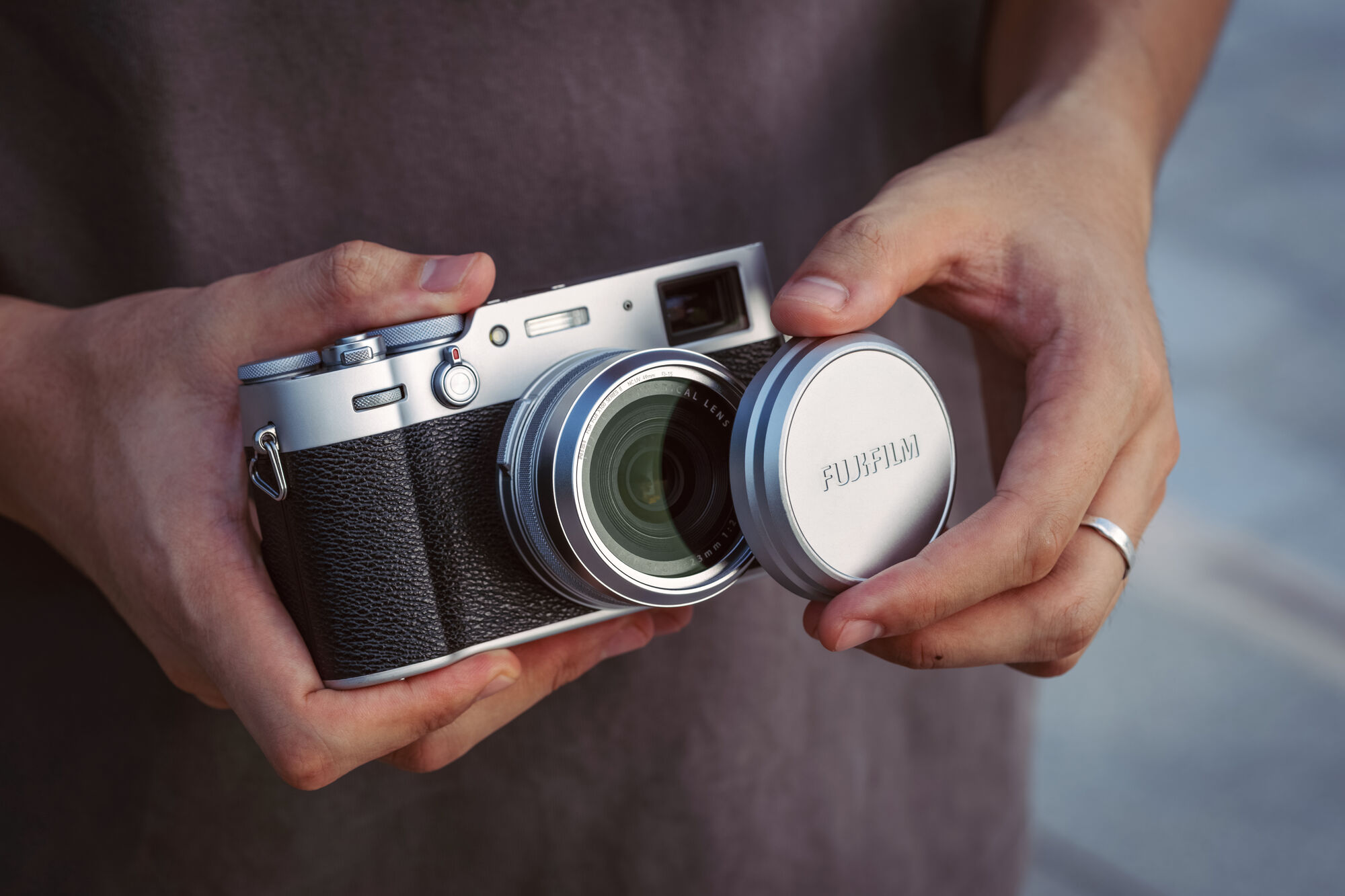 A silver Fujifilm X100 held in both hands with the original Fujifilm lens cap seated on the NiSi filter