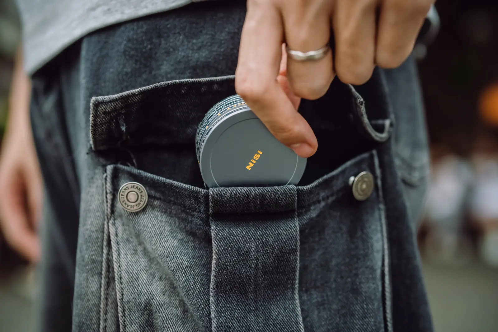 A stack of 49MAG filters and a magnetic cap slipping into a jeans pocket