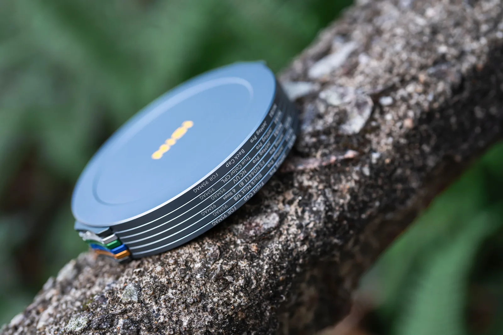 A stack of NiSi JetMag Pro 95MAG filters closed with magnetic caps, resting on a branch