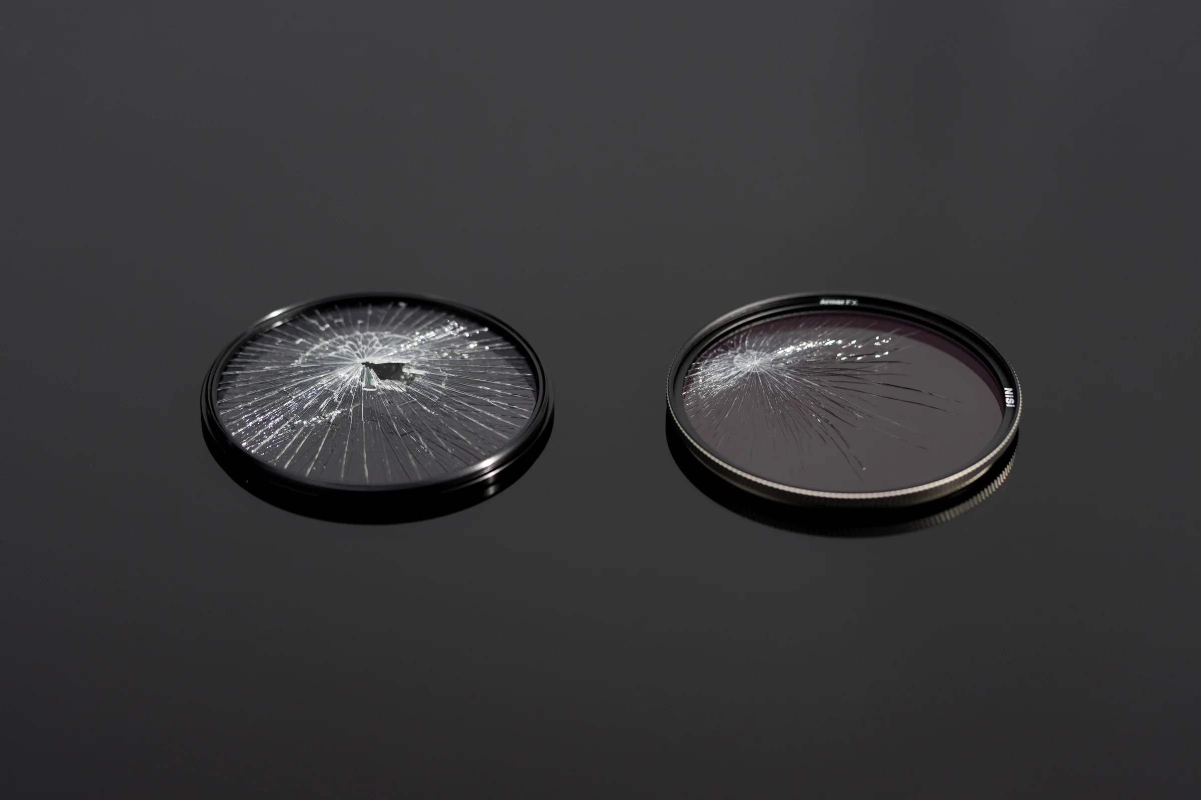 An ordinary UV filter shattered next to a NiSi Armor FX UV filter that has cracked but held together